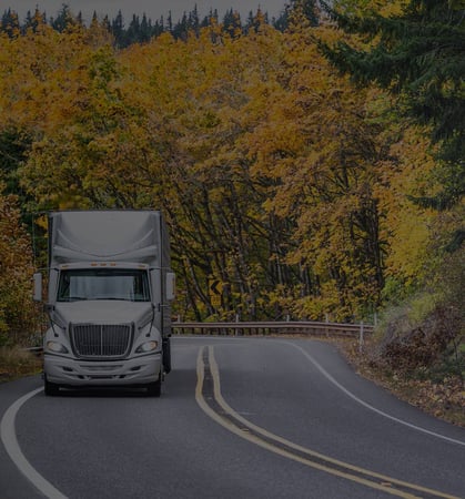 White truck driving up hill with yellow trees